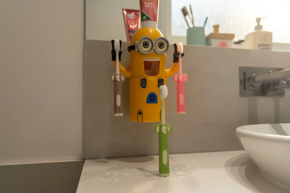 Aussie Kids Toothbrush Co kids toothbrushes in three assorted colours displayed in a fun bathroom lifestyle setting, featuring a character holding two toothbrushes and one toothbrush standing upright with its flat base