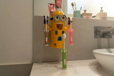 Aussie Kids Toothbrush Co kids toothbrushes in three assorted colours displayed in a fun bathroom lifestyle setting, featuring a character holding two toothbrushes and one toothbrush standing upright with its flat base