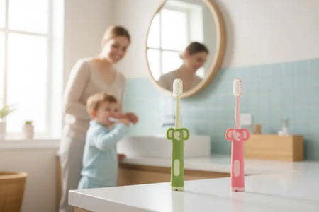 Two Kids Ultra Soft Toothbrushes from the 12-pack standing upright on a bathroom counter, with a mother and child brushing their teeth in the background.
